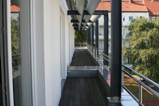 Schmale Holzterrasse mit Geländer entlang der Fassade