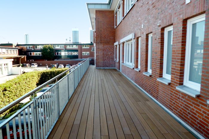 Terrasse aus Holz entlang einer Klinkerfassade mit Geländer