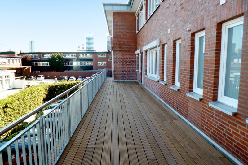 Terrasse aus Holz entlang einer Klinkerfassade mit Geländer